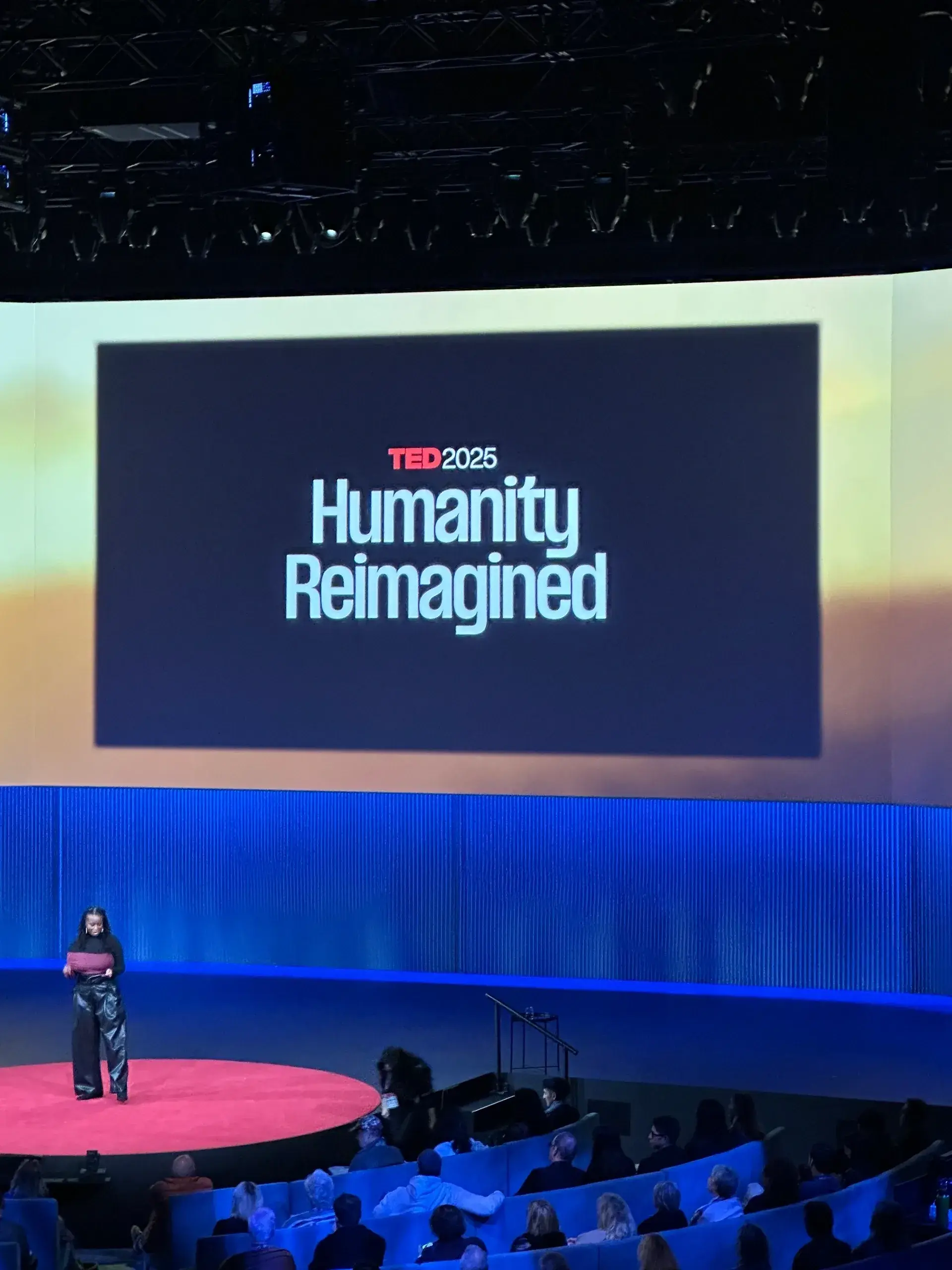 TED Talk stage with "Humanity Reimagined" screen.