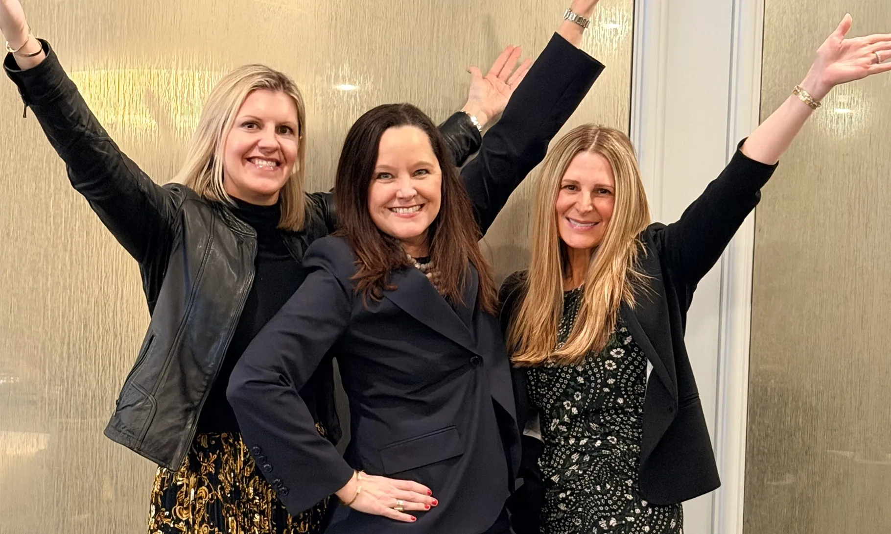 Three smiling women with arms raised